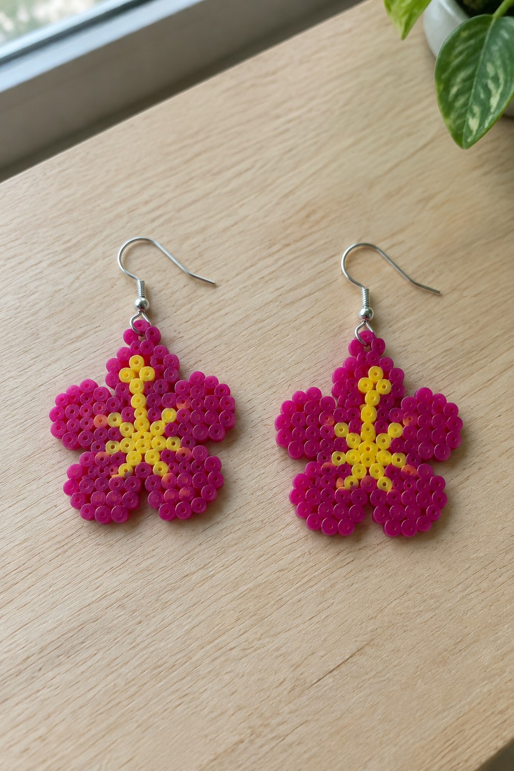 Pair of pink perler bead flower earrings with yellow centers on wood