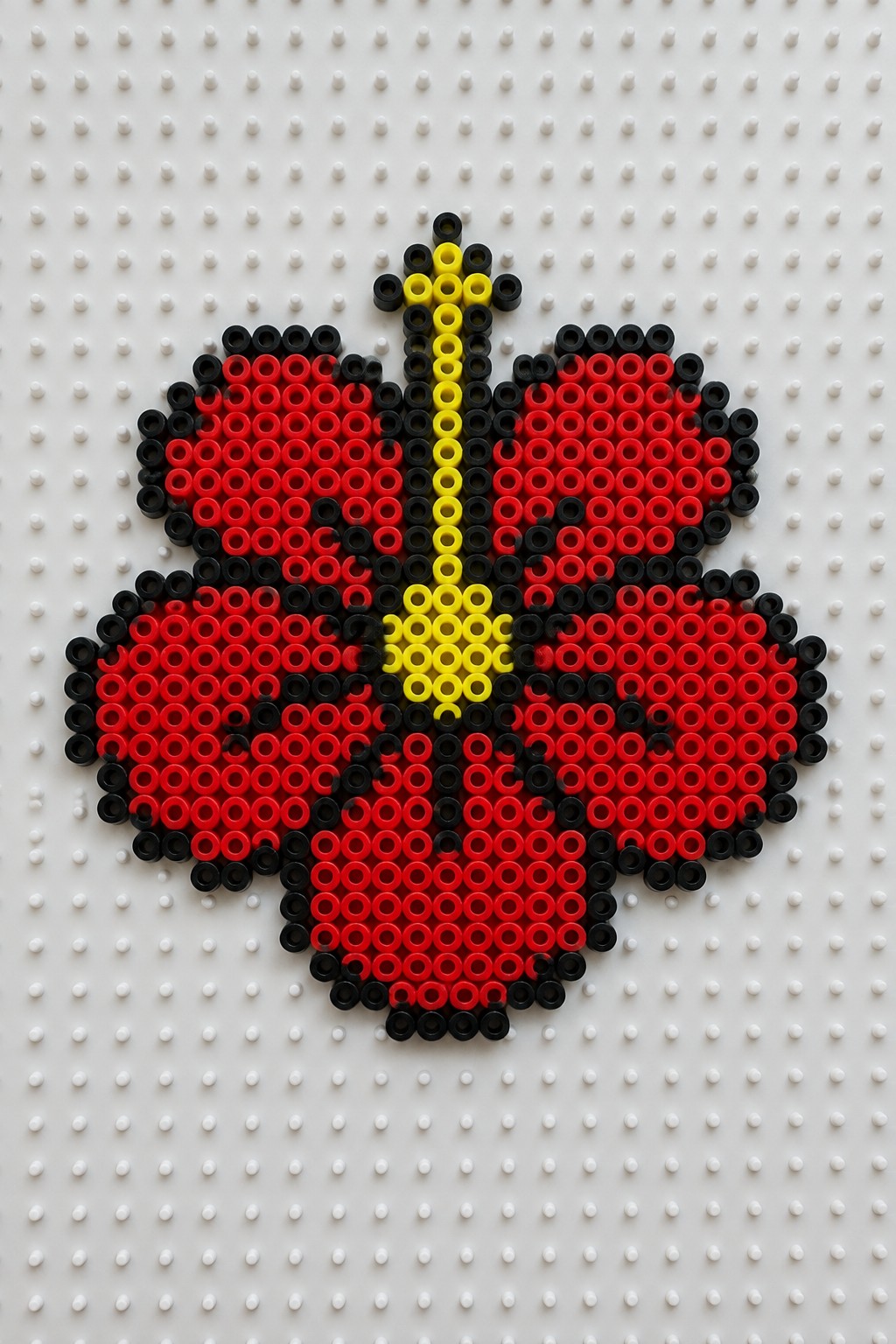 Red perler bead flower with black outline and yellow center on pegboard.