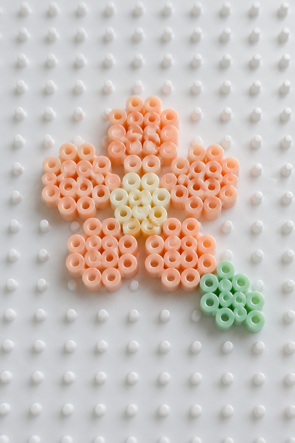 Peach perler bead flower with cream center and green beads on pegboard