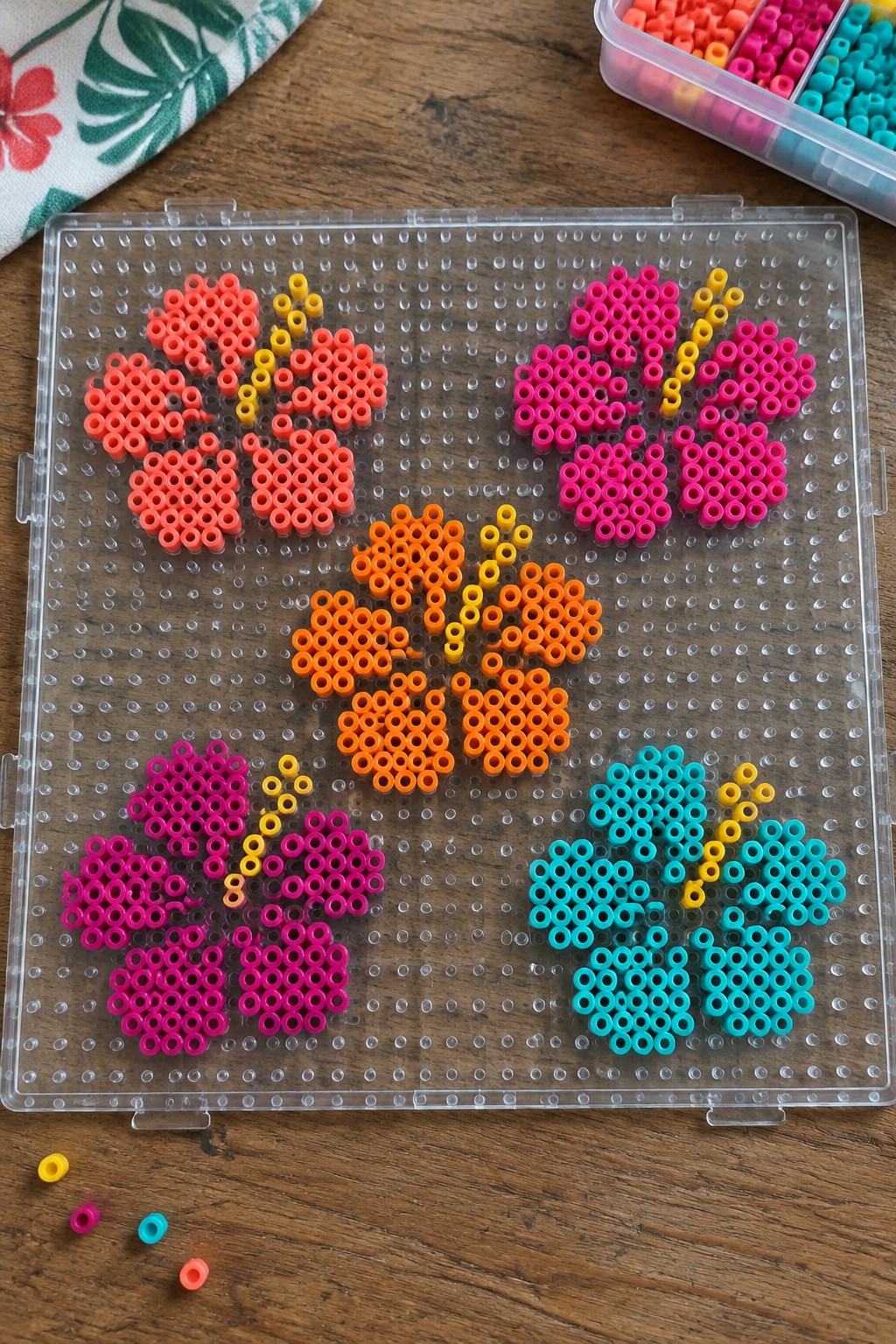 Colorful perler bead flowers arranged on clear pegboard with loose beads nearby