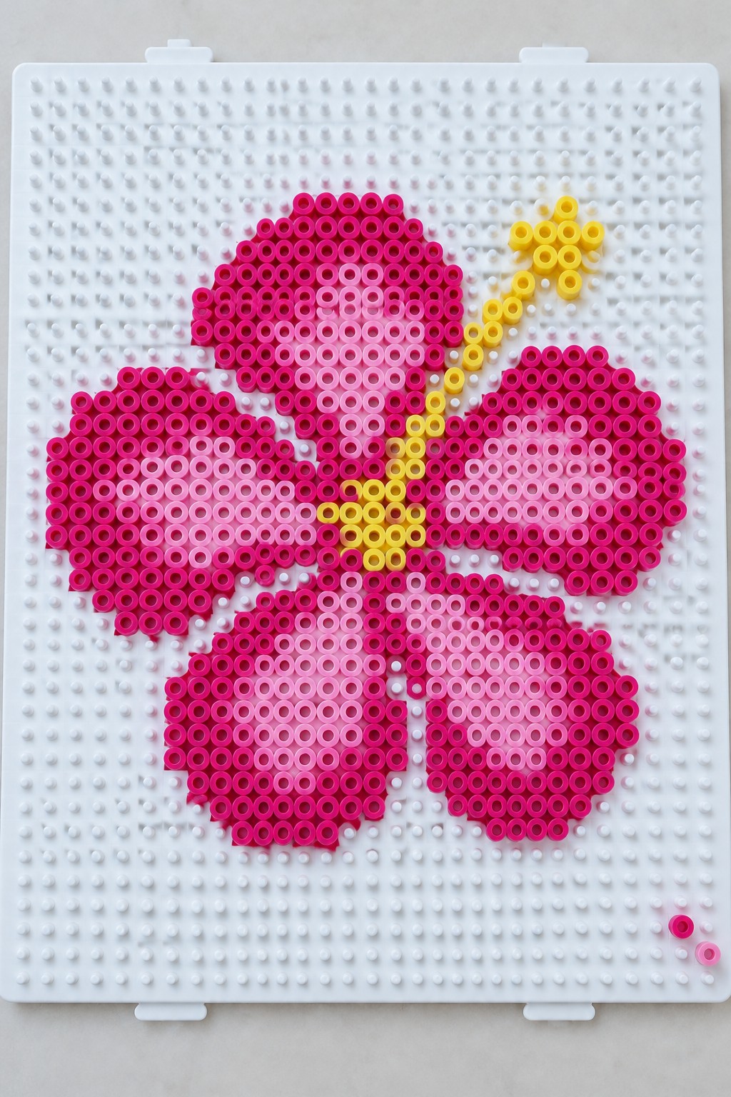 Pink perler bead flower with yellow center on white pegboard