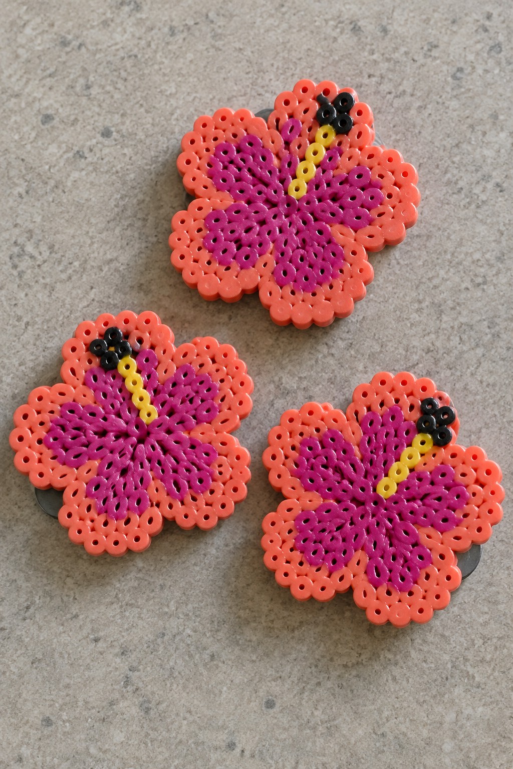 Three perler bead hibiscus flowers in orange, magenta, and yellow.
