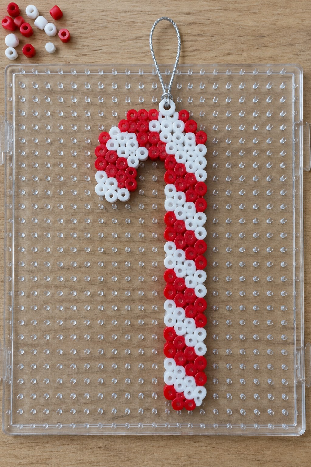 Red and white perler bead candy cane on clear pegboard with silver loop