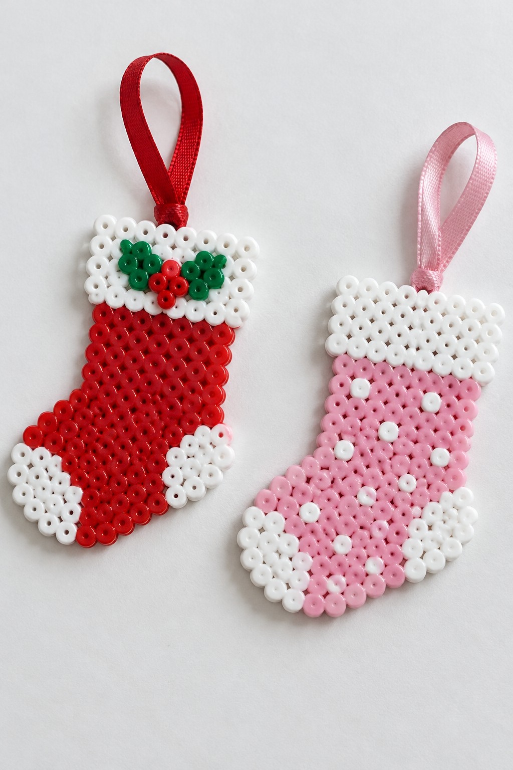 Two red and pink perler bead Christmas stockings with white cuffs and ribbons.