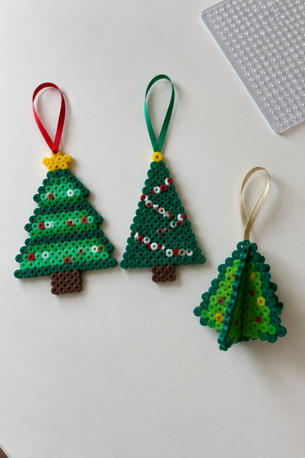 Three perler bead Christmas tree ornaments with red, green, and gold ribbons