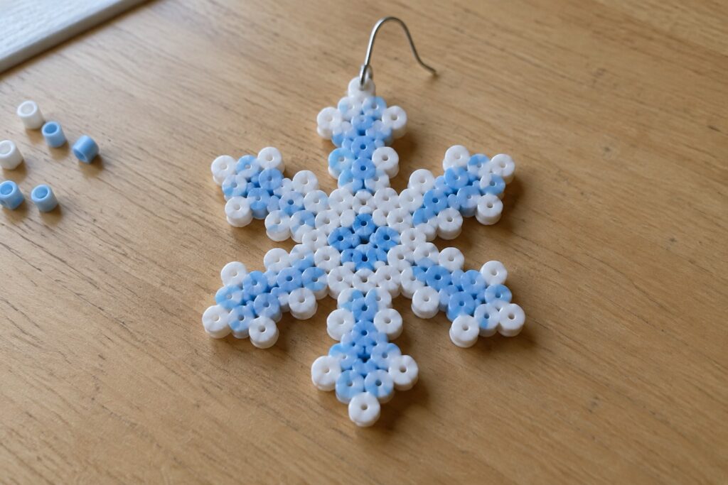 White and blue beaded snowflake earring with silver hook on wood table