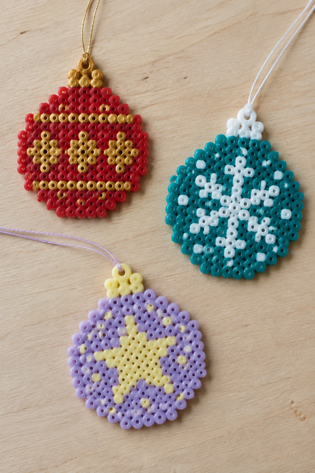 Three perler bead Christmas ornaments with star, snowflake, and geometric patterns on wood.