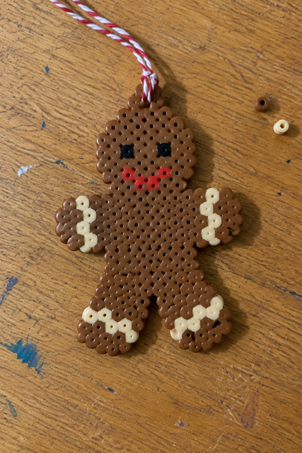 Perler bead gingerbread man with white accents, black eyes, red mouth on wooden table