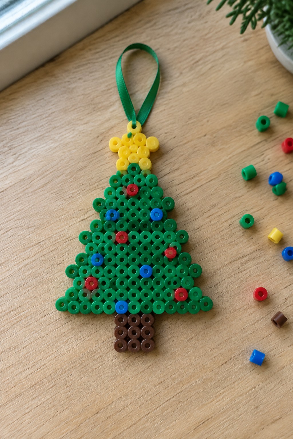 Perler bead Christmas tree ornament with yellow star on wooden table with loose beads