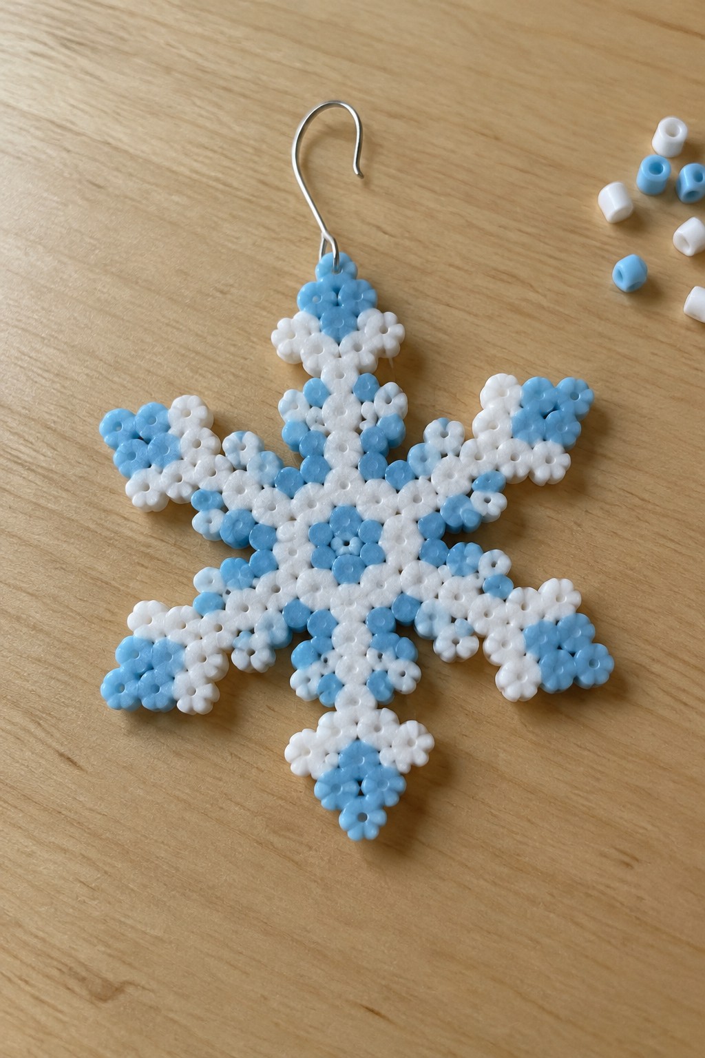 White and blue beaded snowflake earring with silver hook on wood table