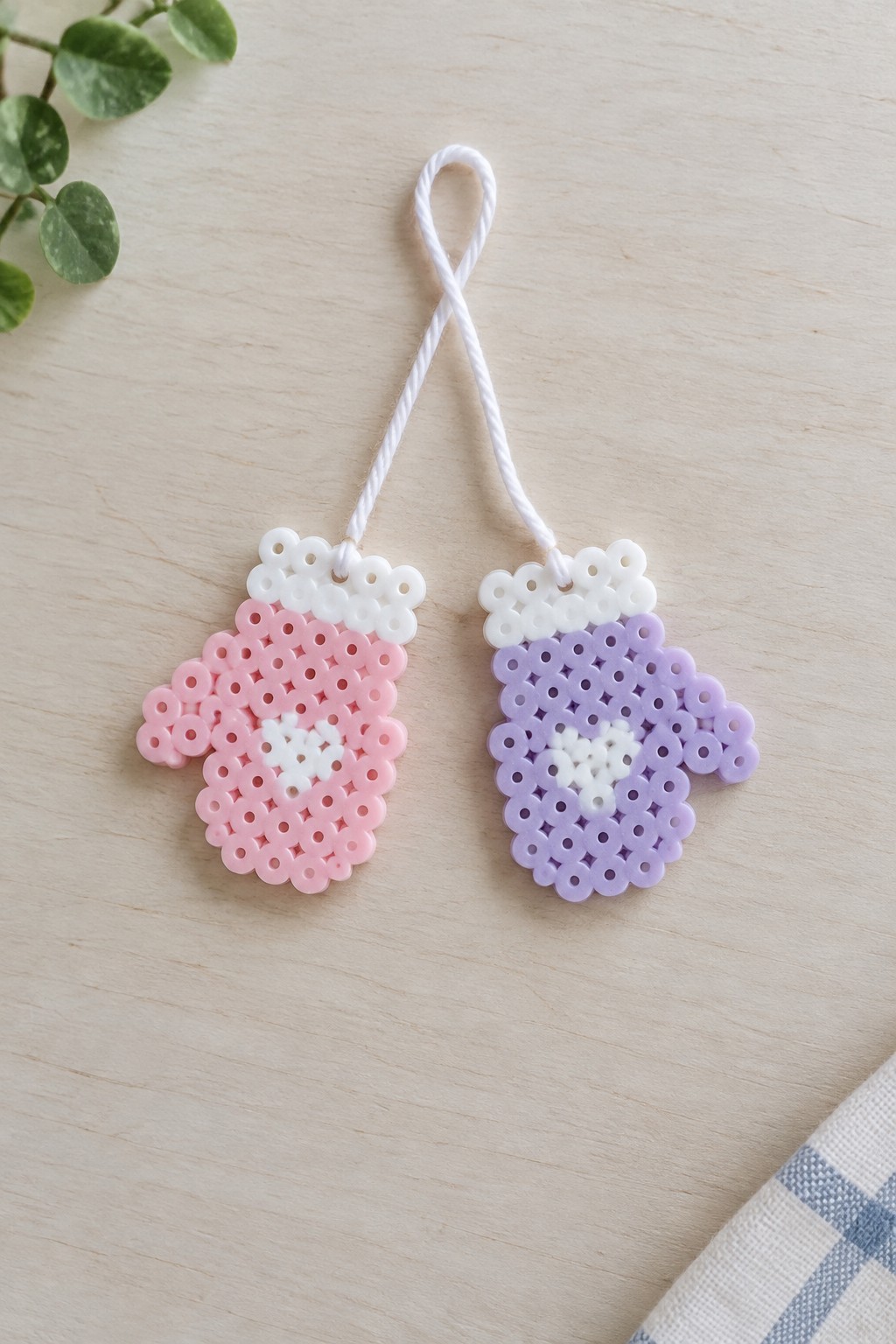 Pink and purple perler bead mittens linked by white cord on wooden table