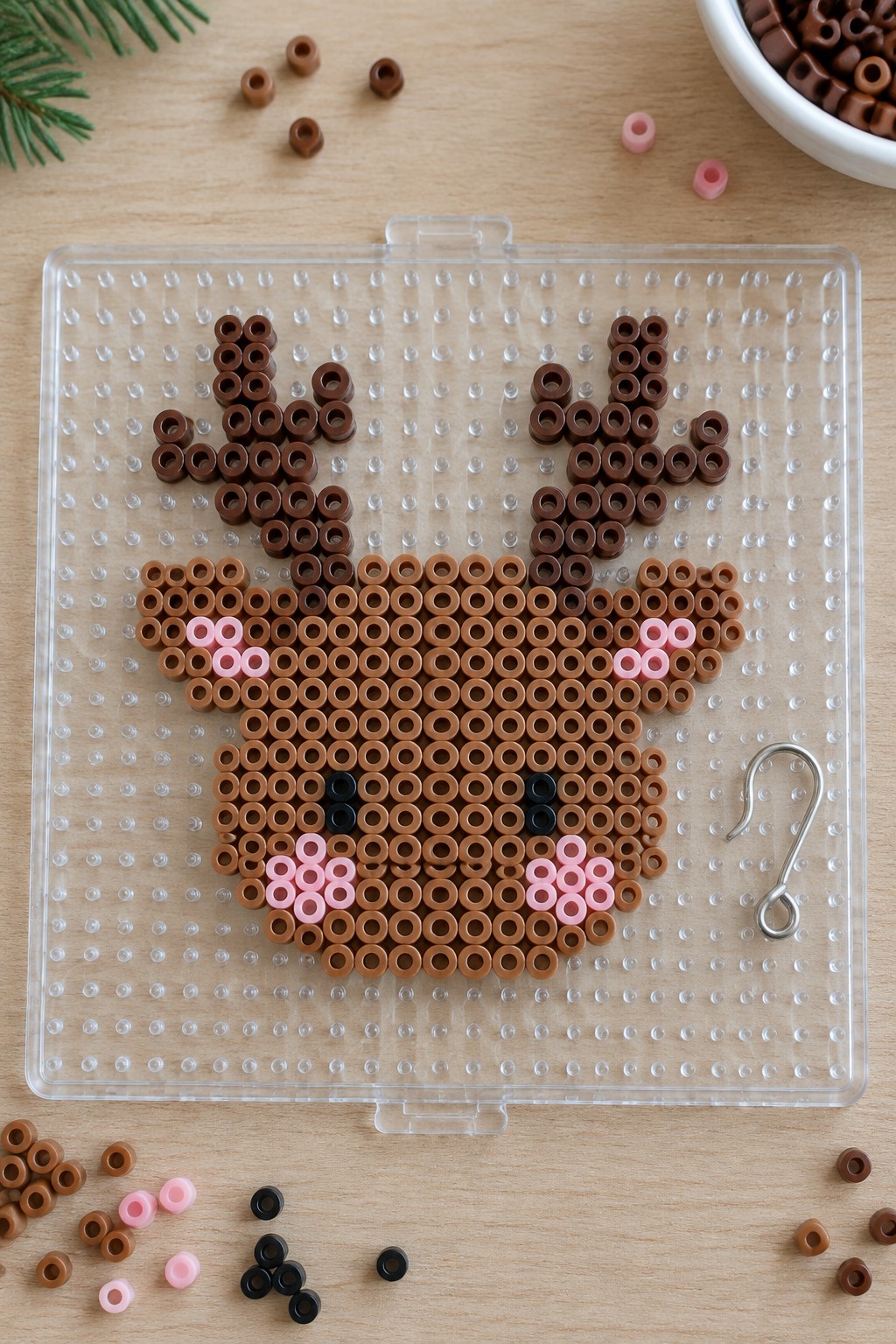 Perler bead reindeer face with brown antlers, pink cheeks on clear pegboard