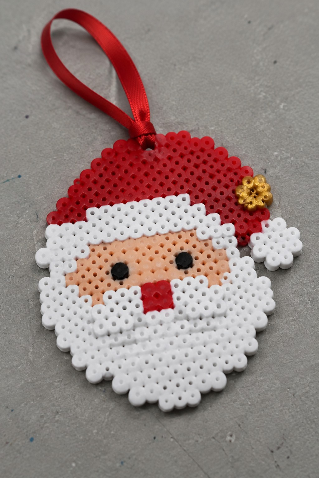 Perler bead Santa Claus ornament with red hat, white beard, and red ribbon
