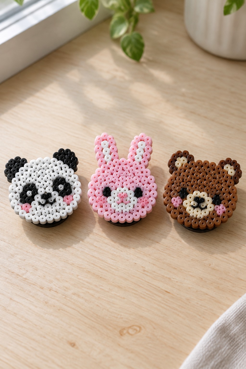 Three perler bead animal faces: panda, pink bunny, and brown bear on wood