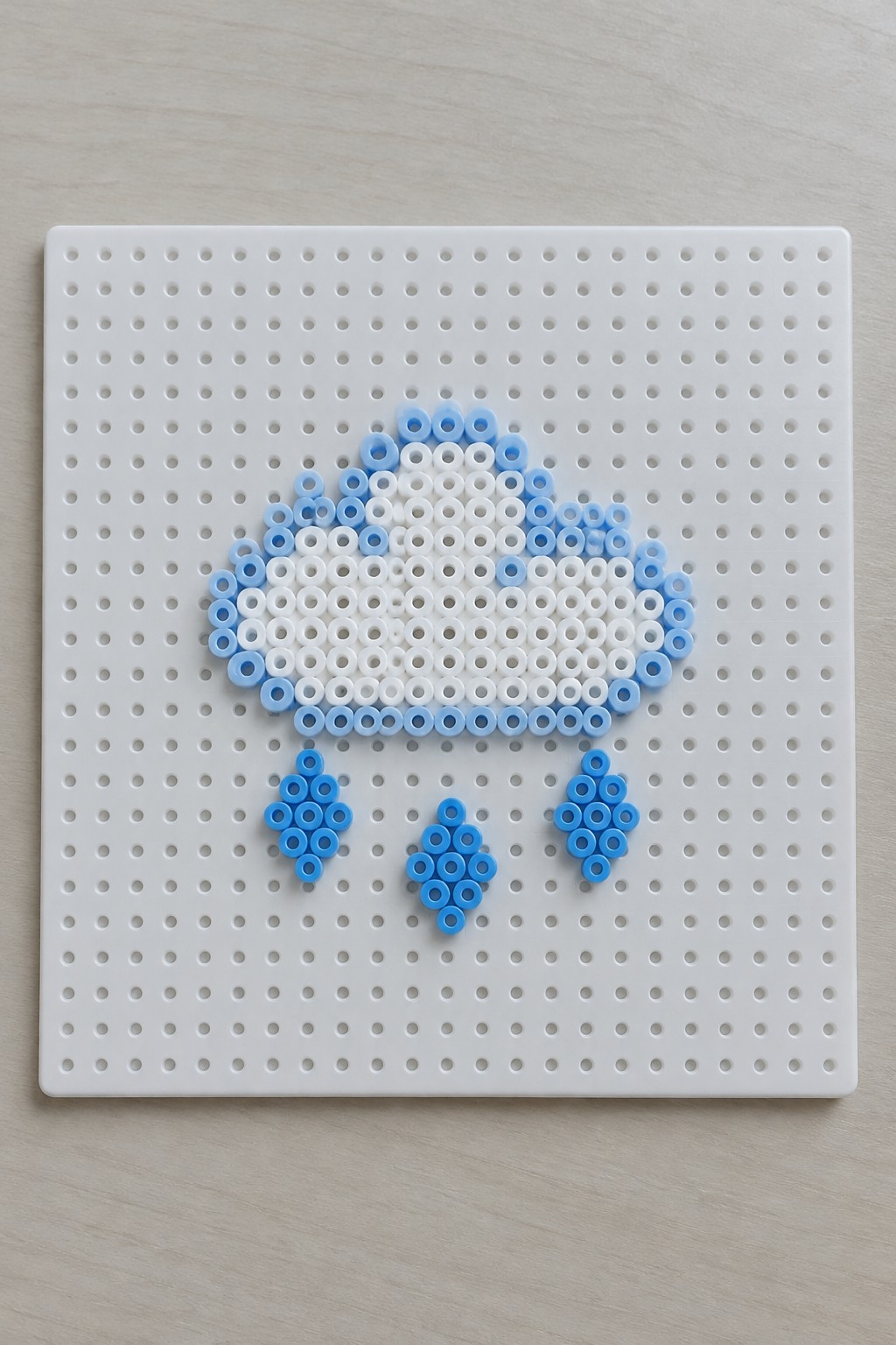Light blue and white beads form a cloud with three raindrops on pegboard.