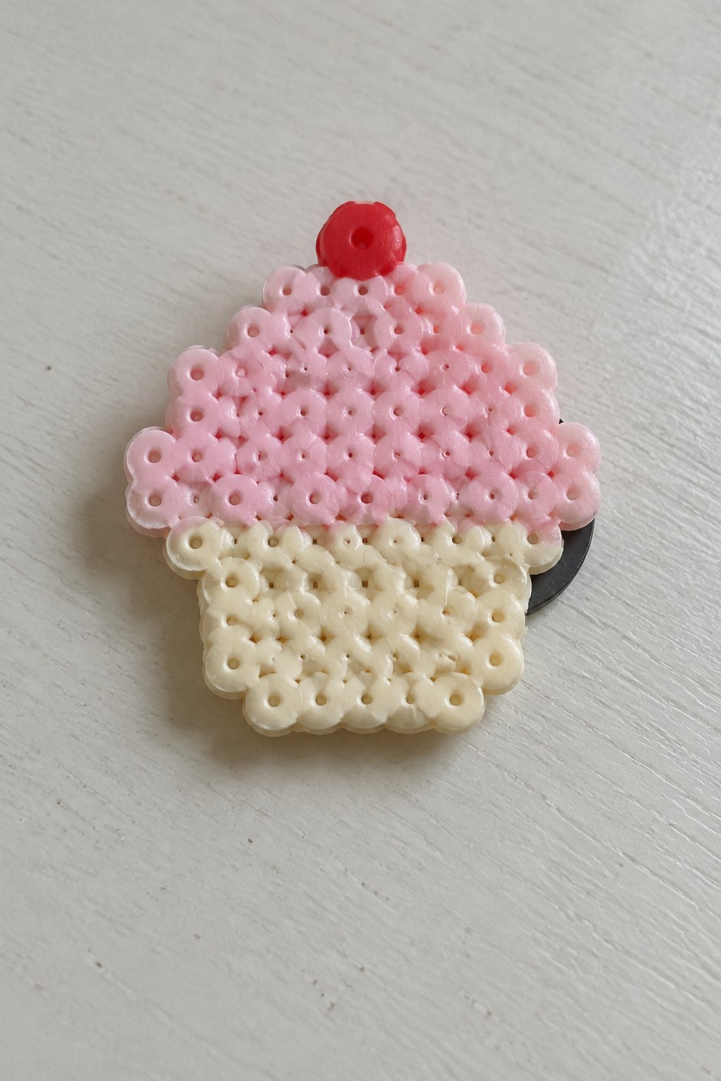 Pink perler bead cupcake with red cherry on light wood surface