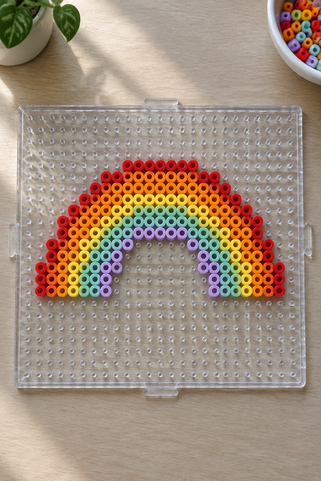 Colorful rainbow made of Perler beads arranged on a clear pegboard.