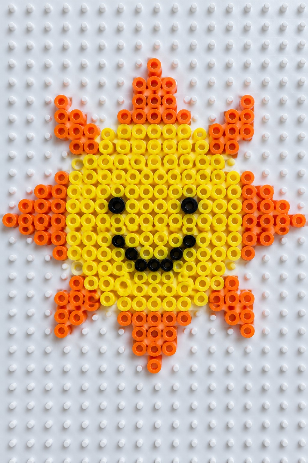 Smiling sun face made from yellow and orange beads on pegboard