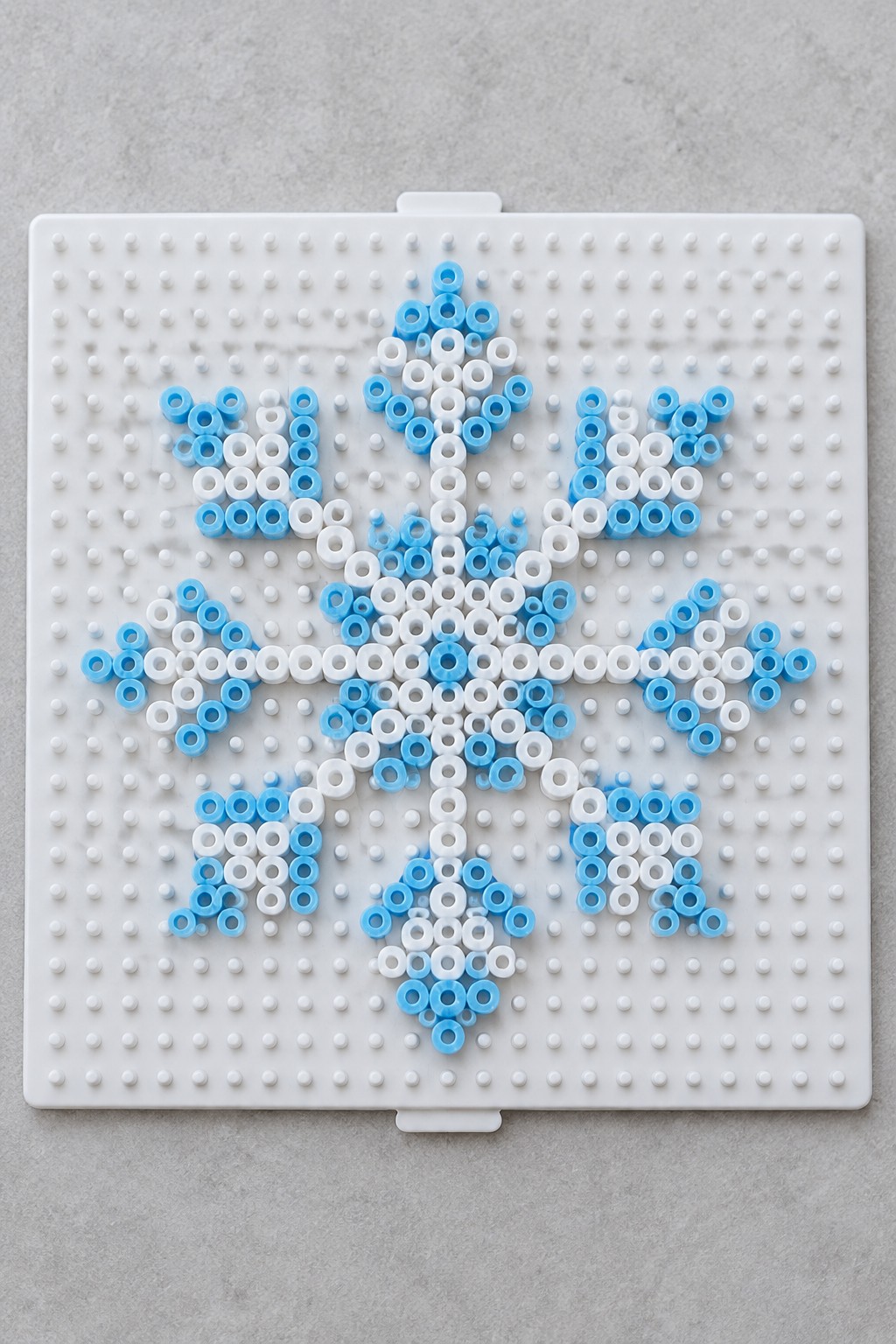 Blue and white beads forming a snowflake on a white pegboard