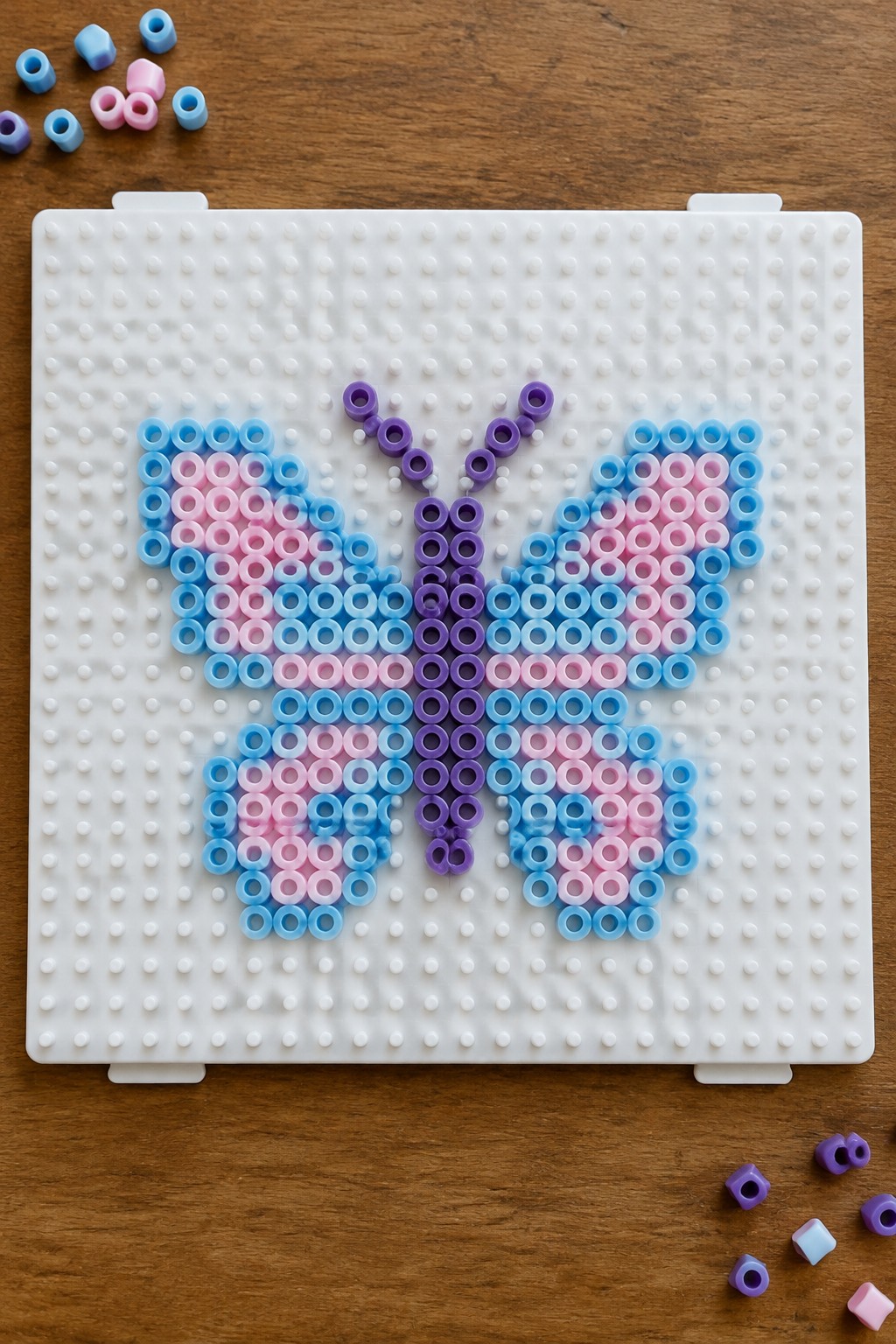 Butterfly made of blue pink purple beads on white pegboard with loose beads nearby