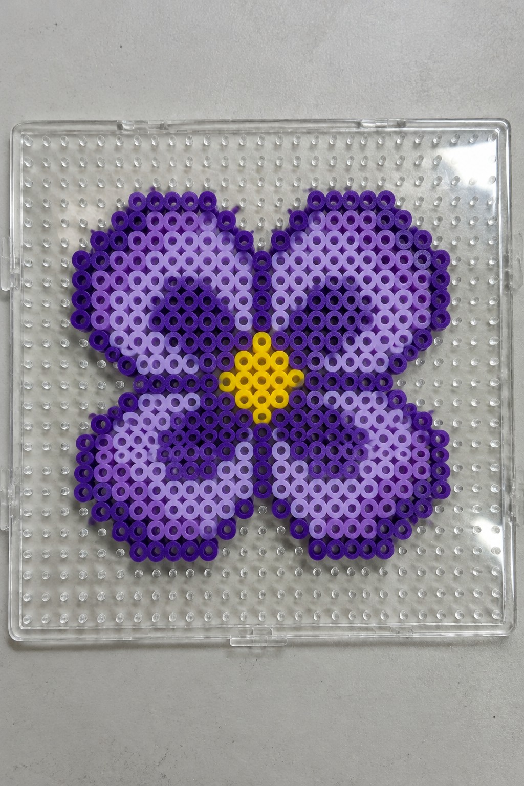 Perler bead butterfly with purple gradient wings and yellow body arranged on a pegboard.
