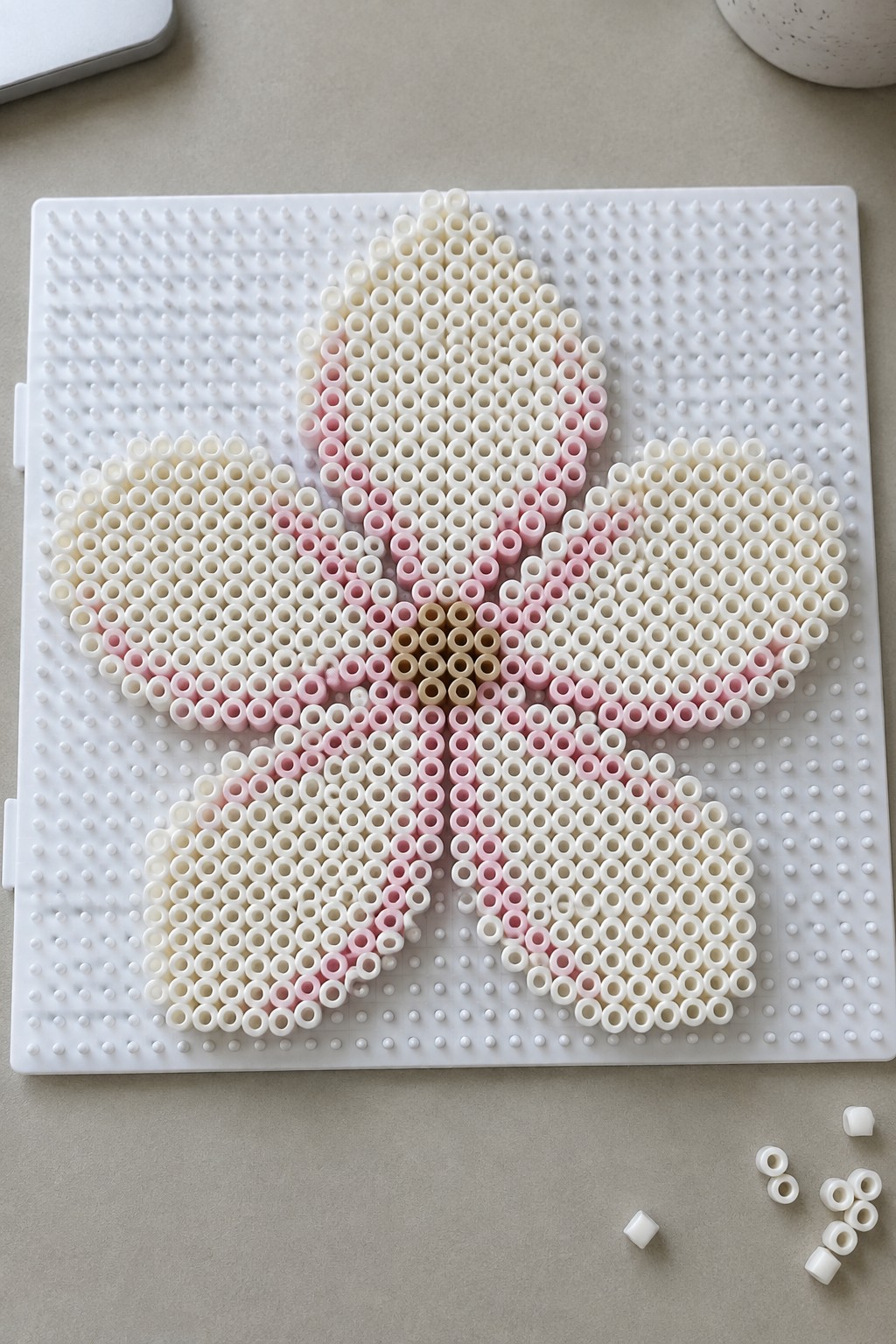 Pink and white perler beads forming a flower on a white pegboard.