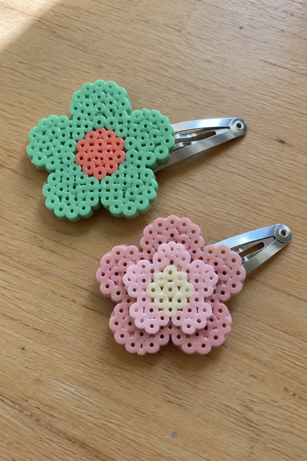 Mint green and pink perler bead flower hair clips on wood.