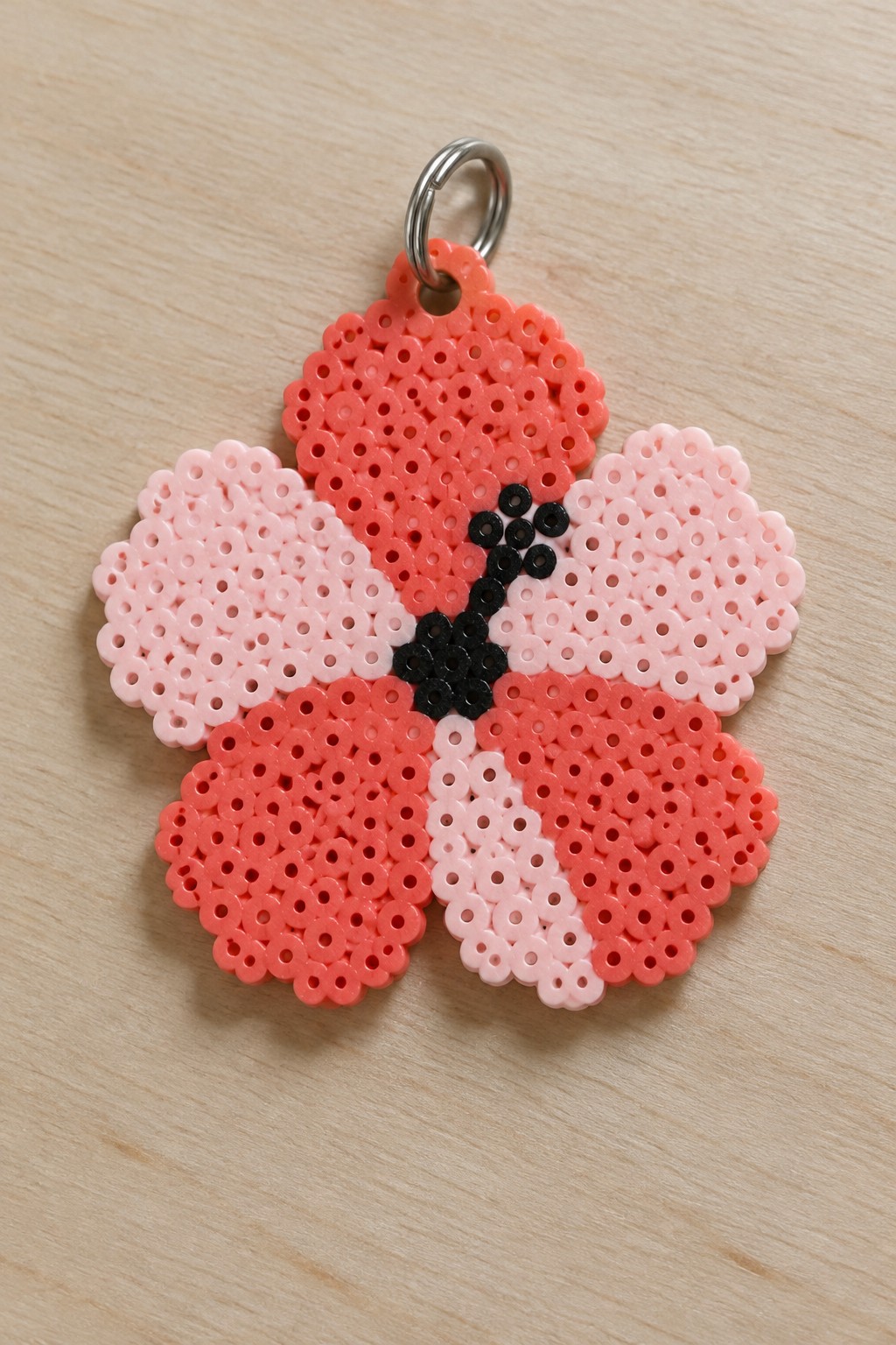 Perler bead flower keychain with five pink and coral petals and black center attached to a metal ring.