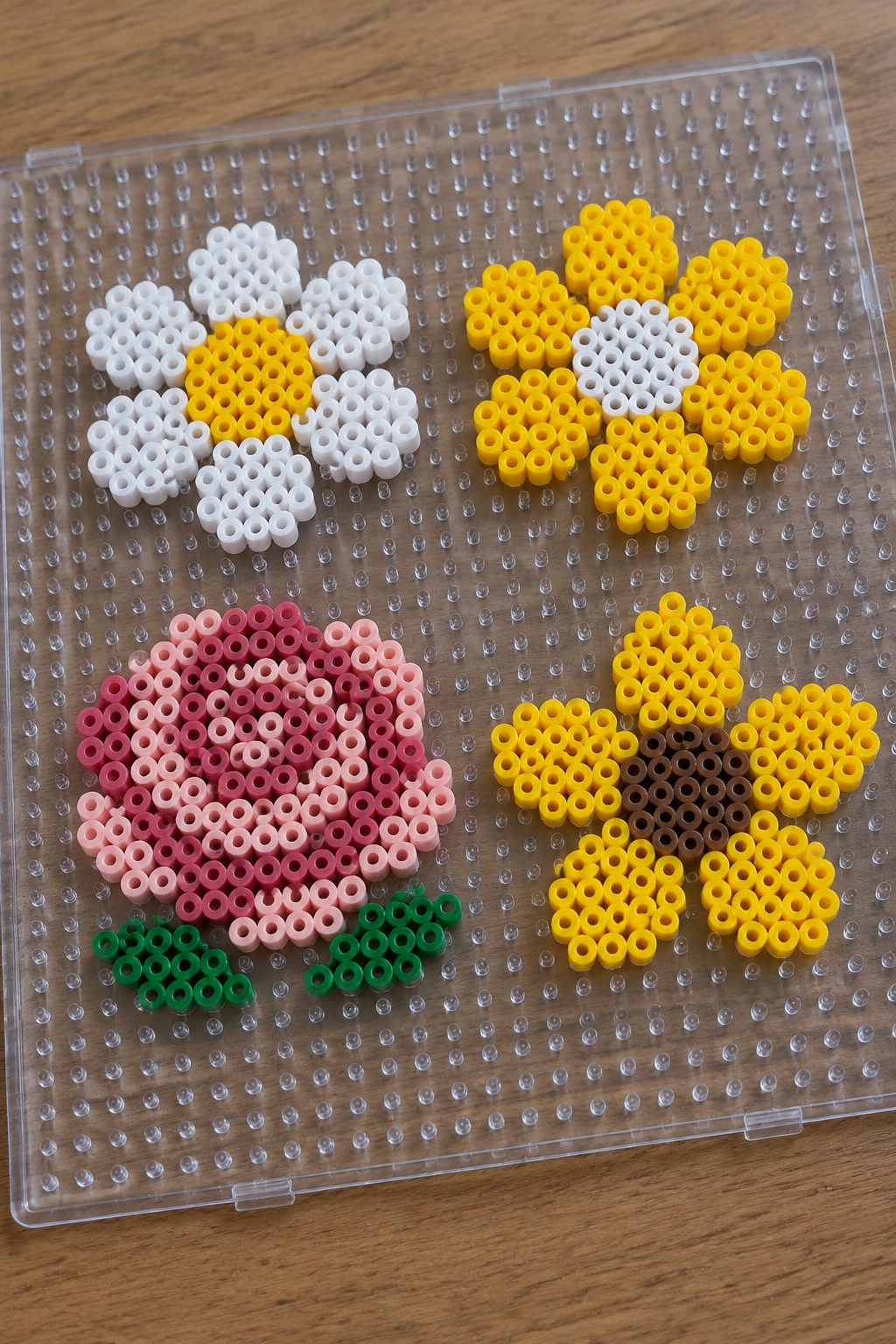 Four perler bead flowers in pink, yellow, white on clear pegboard.
