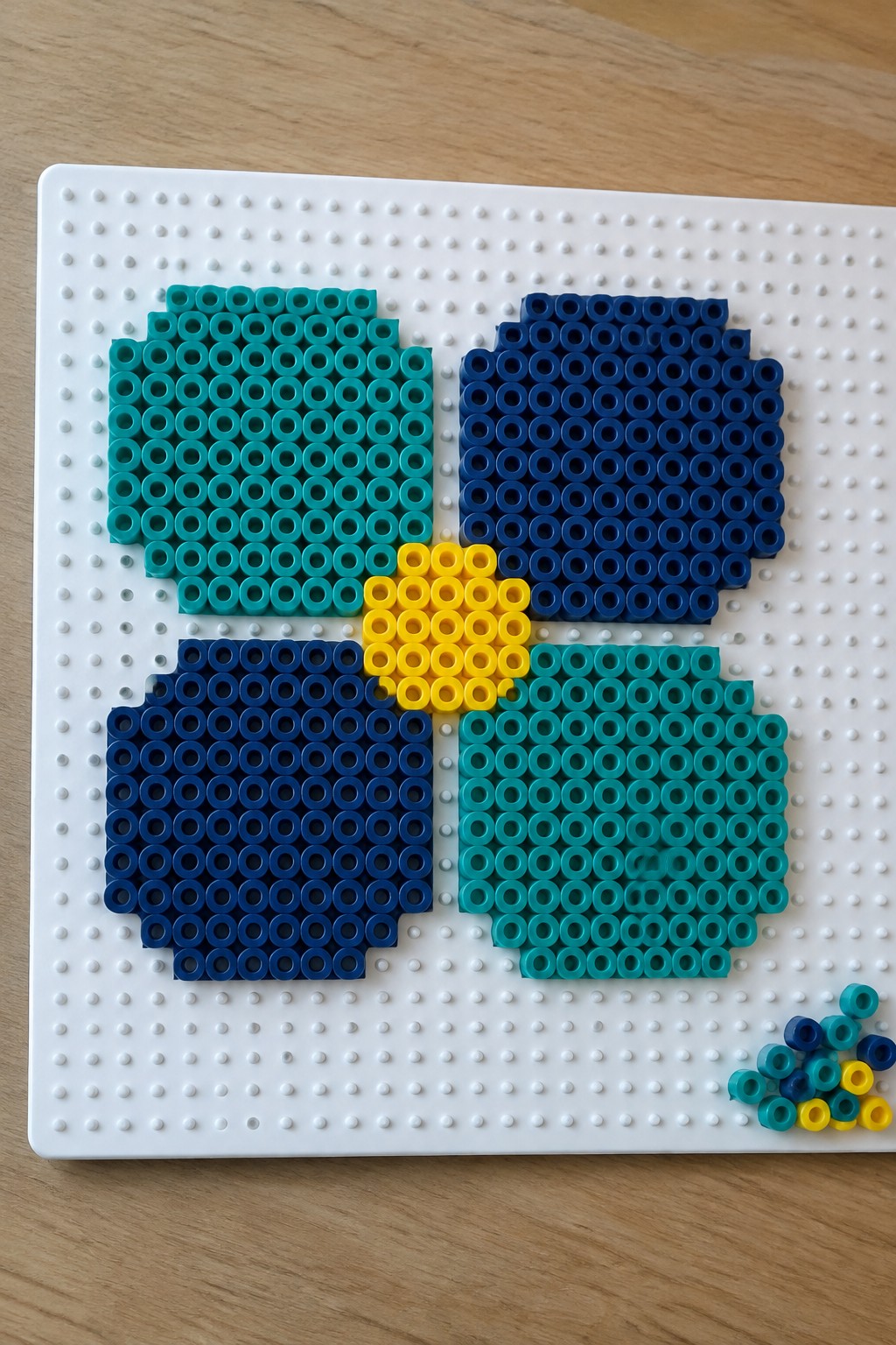 Teal, blue, and yellow Perler beads forming shapes on white pegboard.