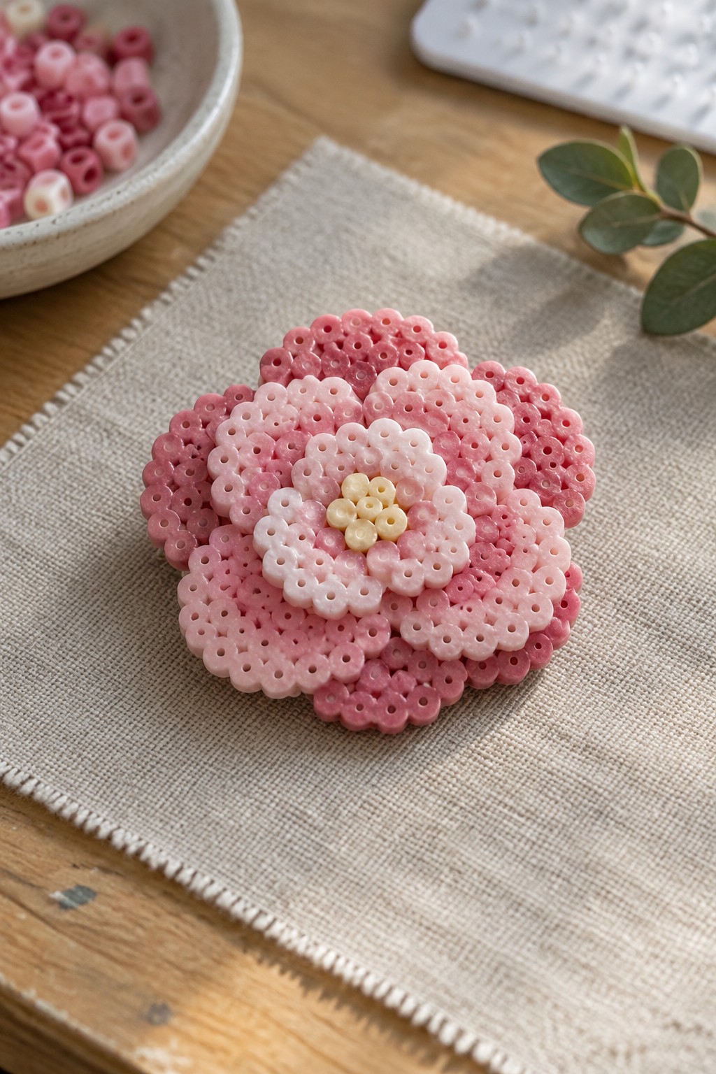 Pink gradient perler bead flower with yellow center on beige linen fabric