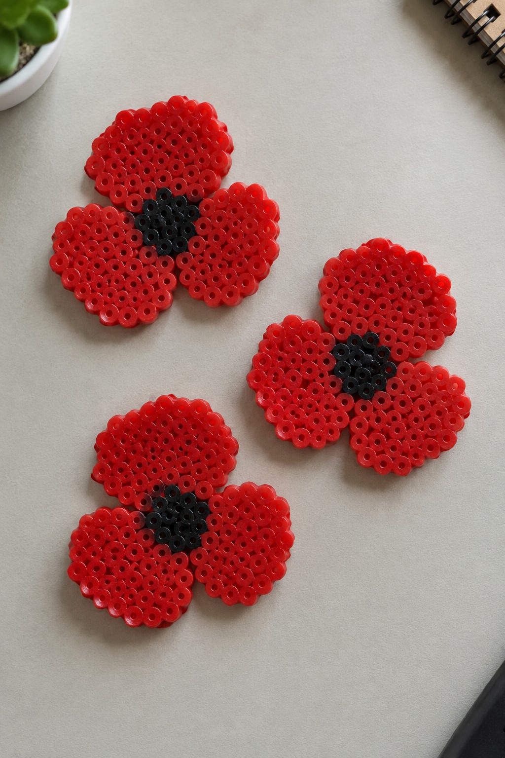 Four red beaded poppy flowers with black centers on a light surface
