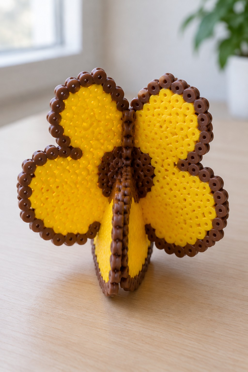 Yellow and brown perler bead butterfly standing on wooden table