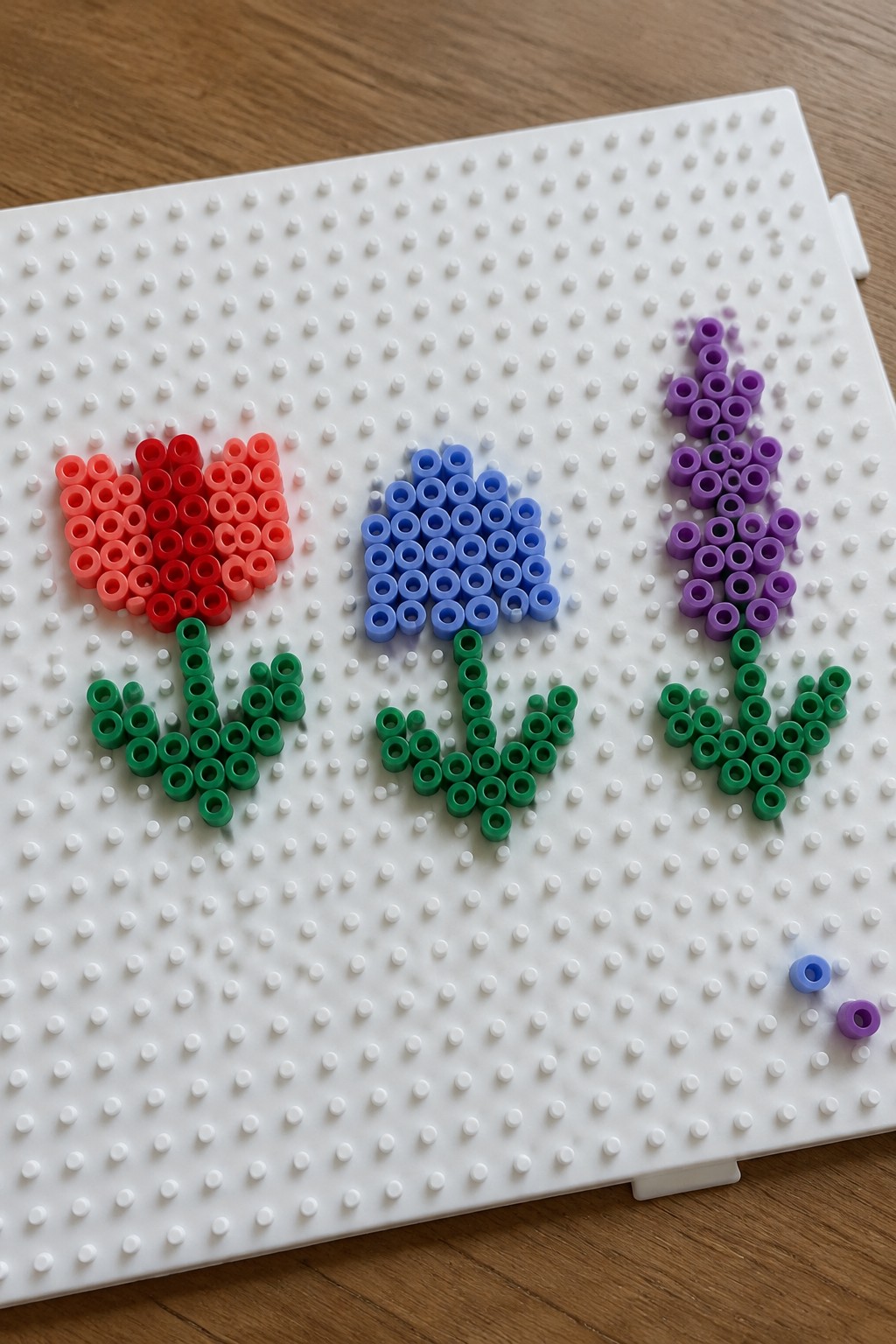 Three perler bead flowers in red, blue, and purple on white pegboard.