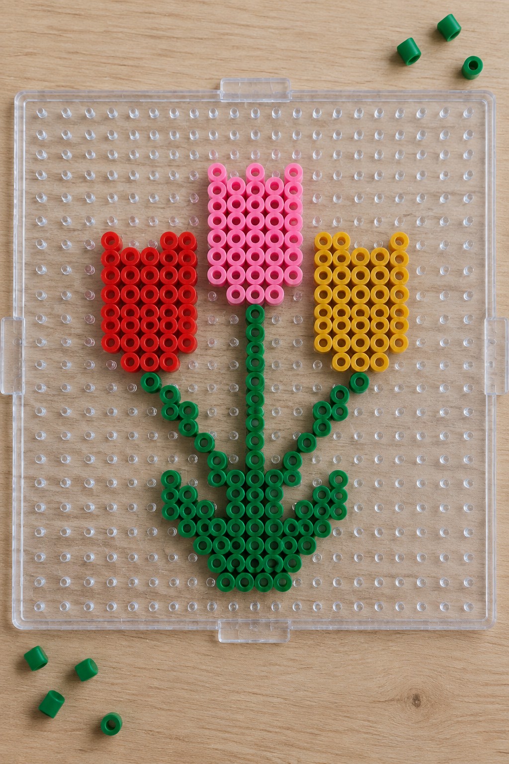 Three tulips formed from red, pink, and yellow beads on a pegboard