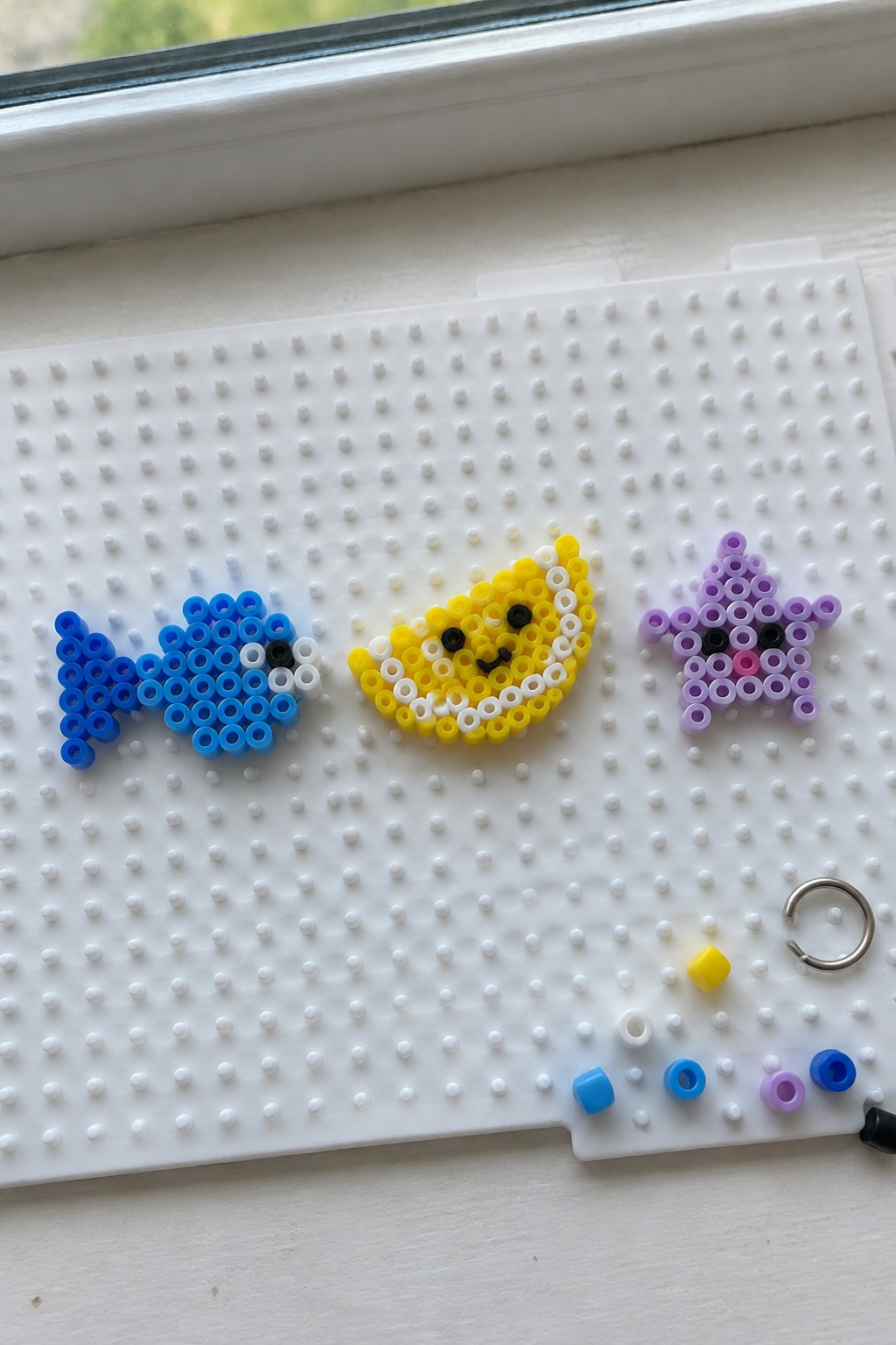 Blue fish, yellow moon face, and purple star perler beads on pegboard.