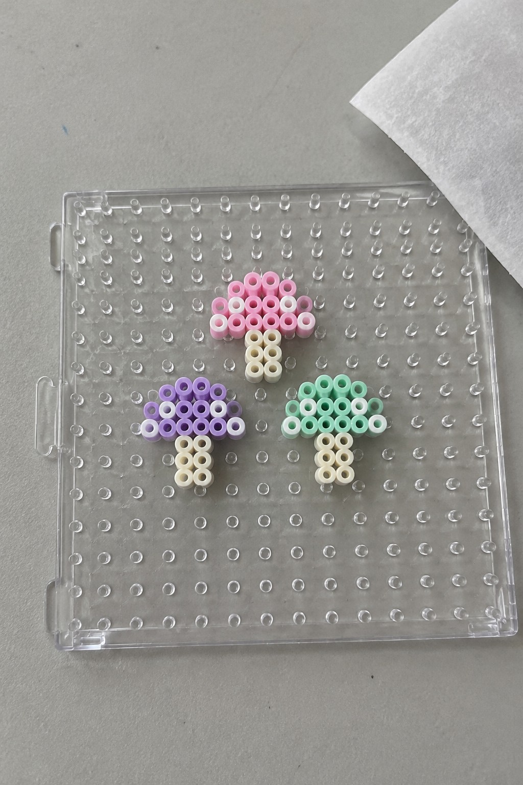 Three perler bead mushrooms in pink, purple, and green on pegboard