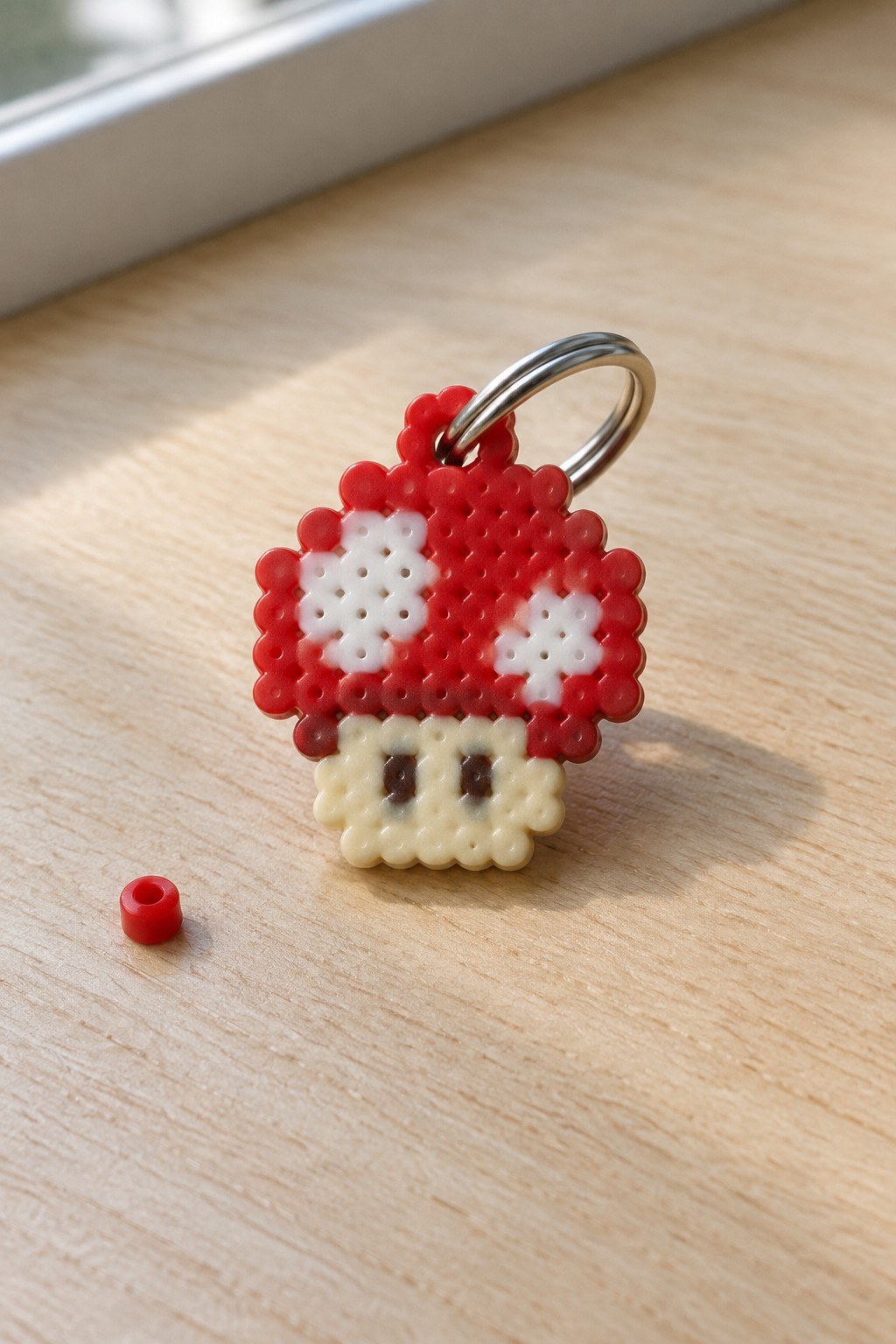 Perler bead Mario mushroom keychain on wood beside small red bead