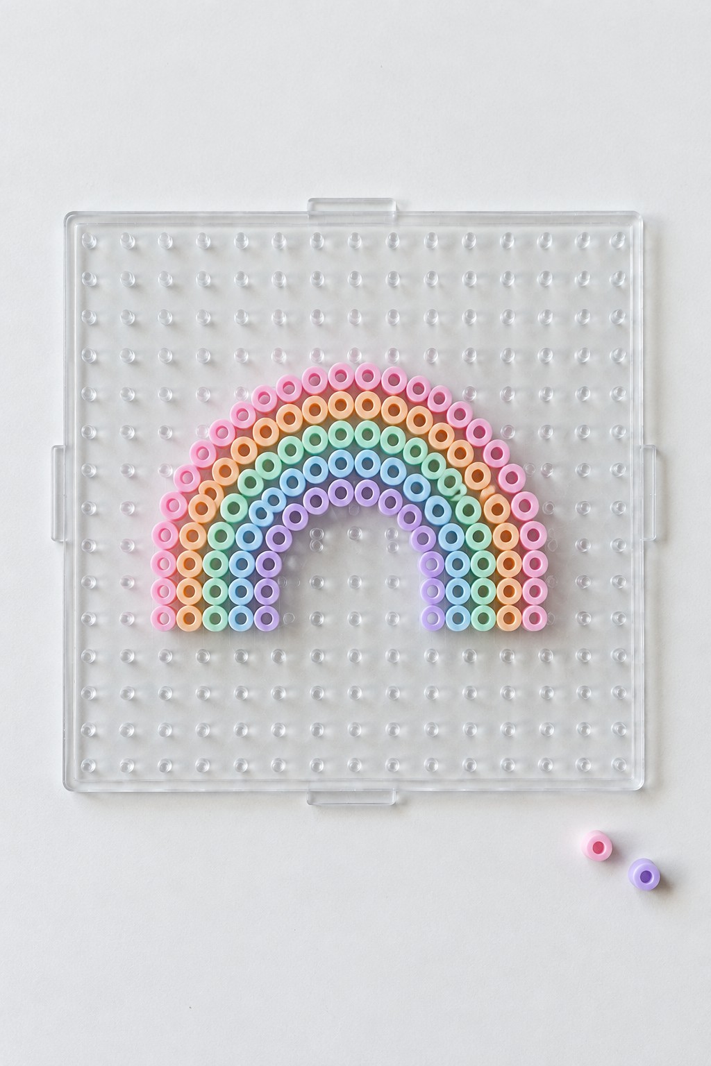 Pastel bead rainbow arranged on clear pegboard with two loose beads nearby