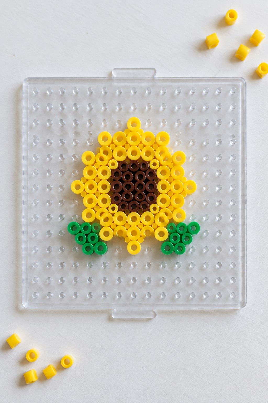 Yellow sunflower perler bead art with brown center and green leaves on pegboard