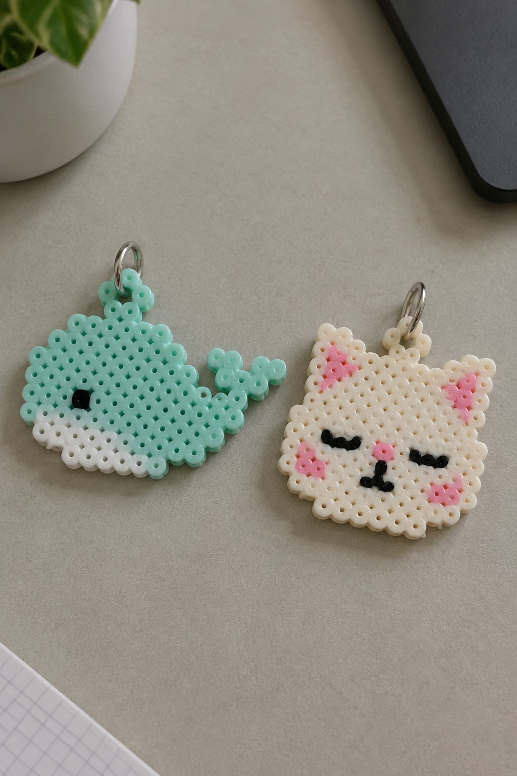 Mint green whale and cream cat perler bead keychains on gray surface