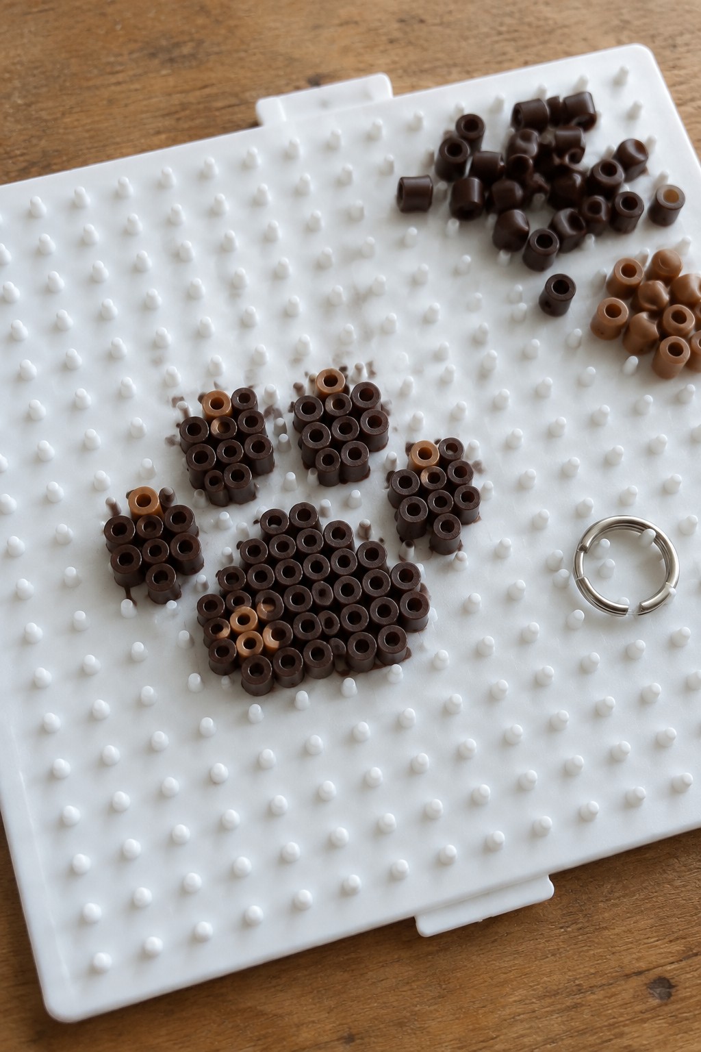 Multiple unfused Perler bead paw prints in dark brown and tan on a white pegboard.