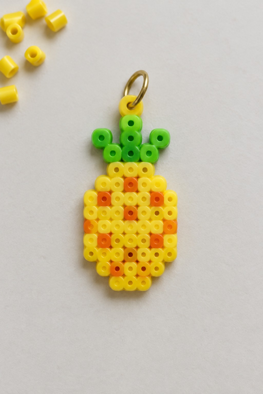 Yellow perler bead pineapple charm with orange accents, green top, and gold ring.