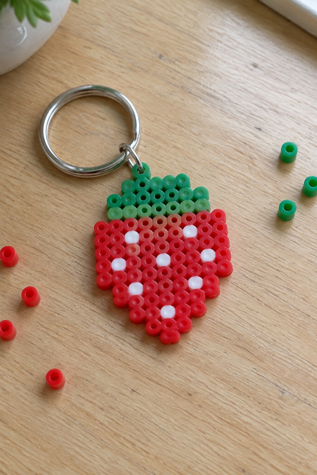 Strawberry Perler bead keychain with red body, white seeds, green top on wood.