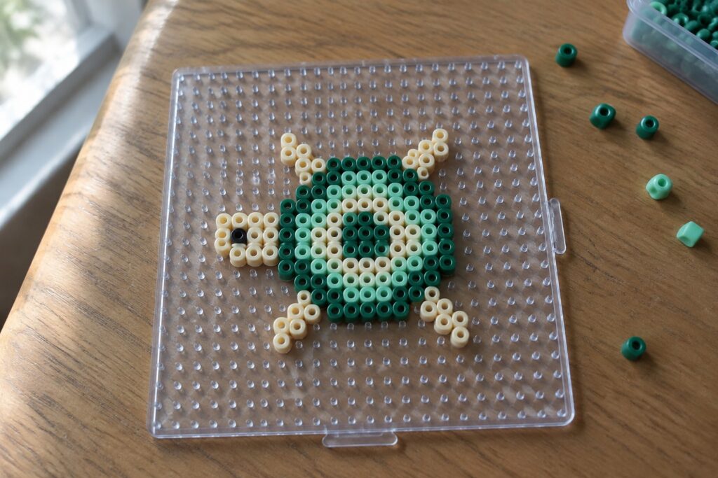 21 Mini Perler Bead Ideas for Tiny Animal Patterns Green and beige perler beads forming a turtle on a clear pegboard with loose beads nearby