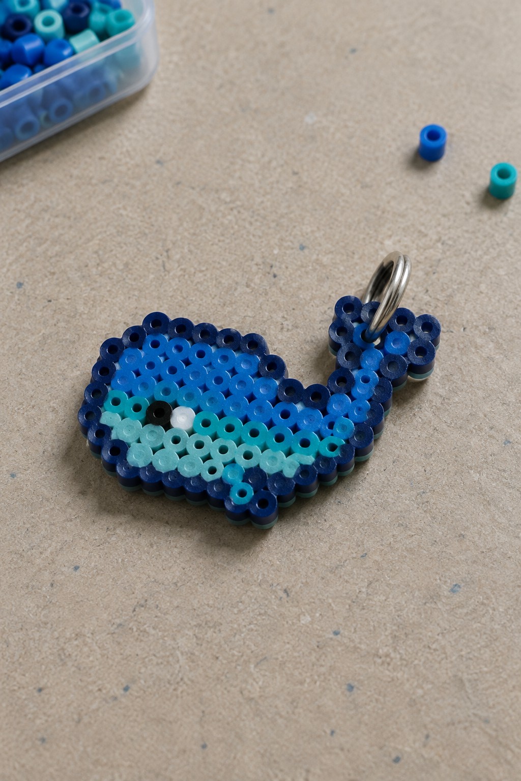 Blue perler bead whale keychain with metal ring on beige surface