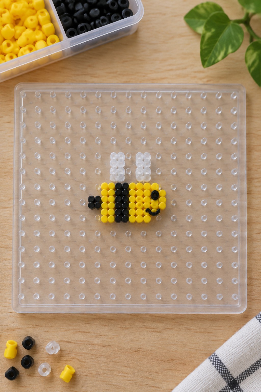 Yellow and black perler bead bee with white wings on clear pegboard