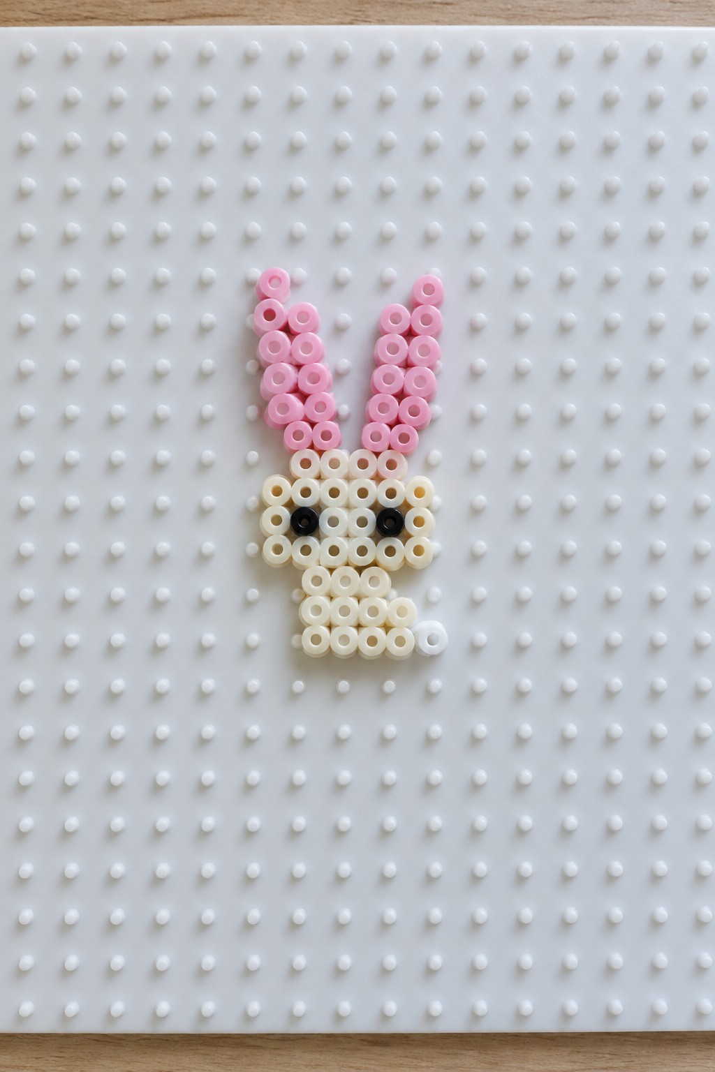 Perler bead bunny with pink ears, white face, and black eyes on pegboard