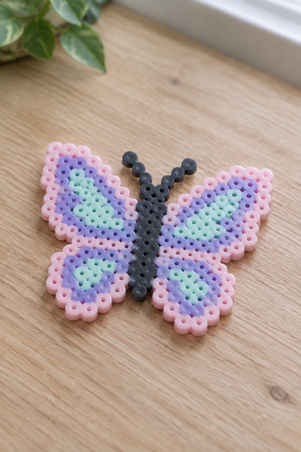 Pink purple mint perler bead butterfly with black body on wooden table