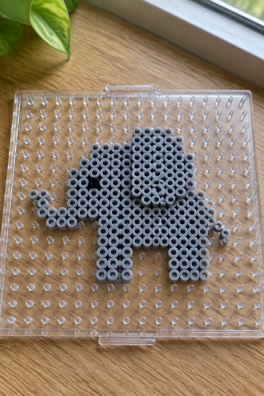 Gray perler beads forming elephant shape with black eye on pegboard